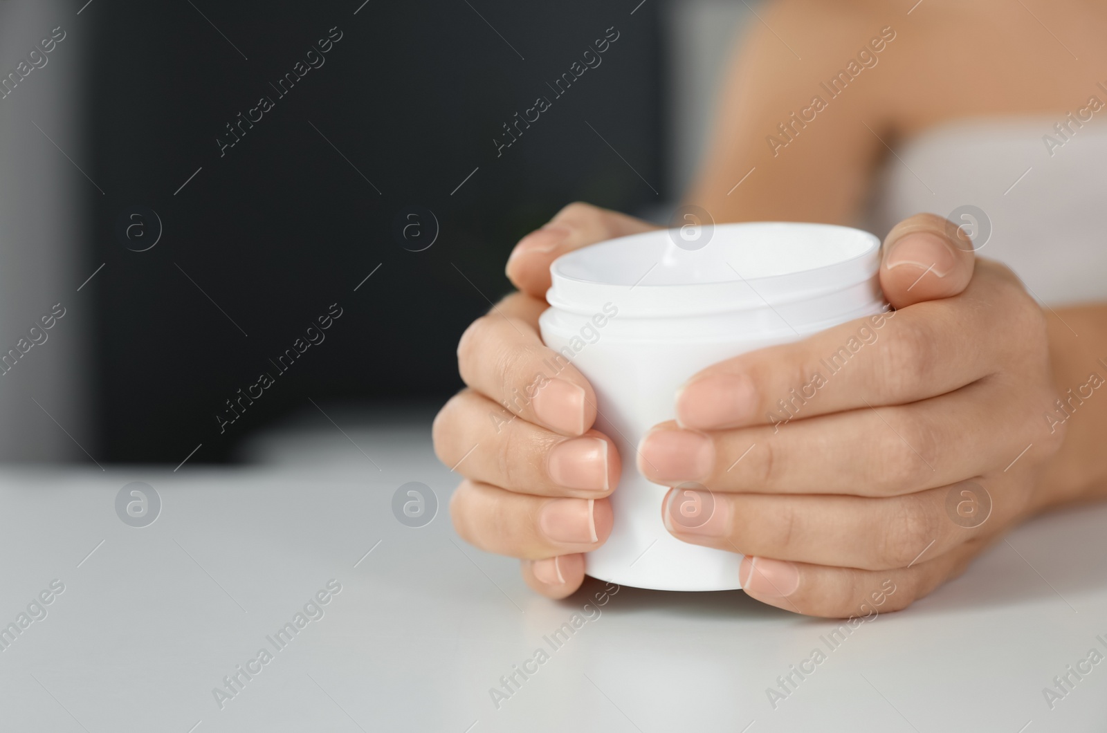 Photo of Woman with jar of moisturizing cream at white table, closeup. Space for text