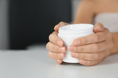 Woman with jar of moisturizing cream at white table, closeup. Space for text