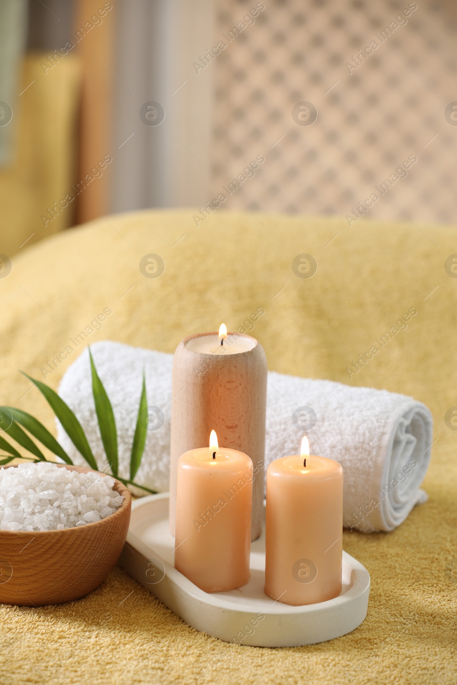 Photo of Spa composition. Burning candles, sea salt and towel on soft yellow surface