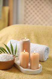 Spa composition. Burning candles, sea salt and towel on soft yellow surface