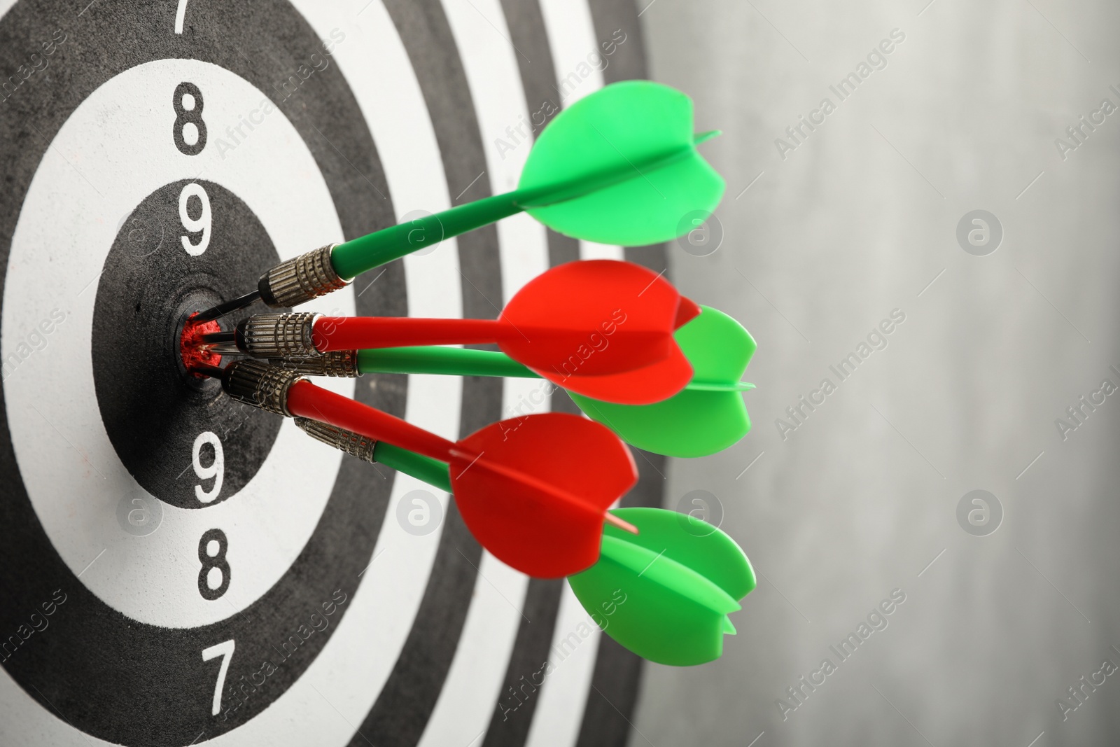 Photo of Dart board with arrows hitting target on grey wall, closeup