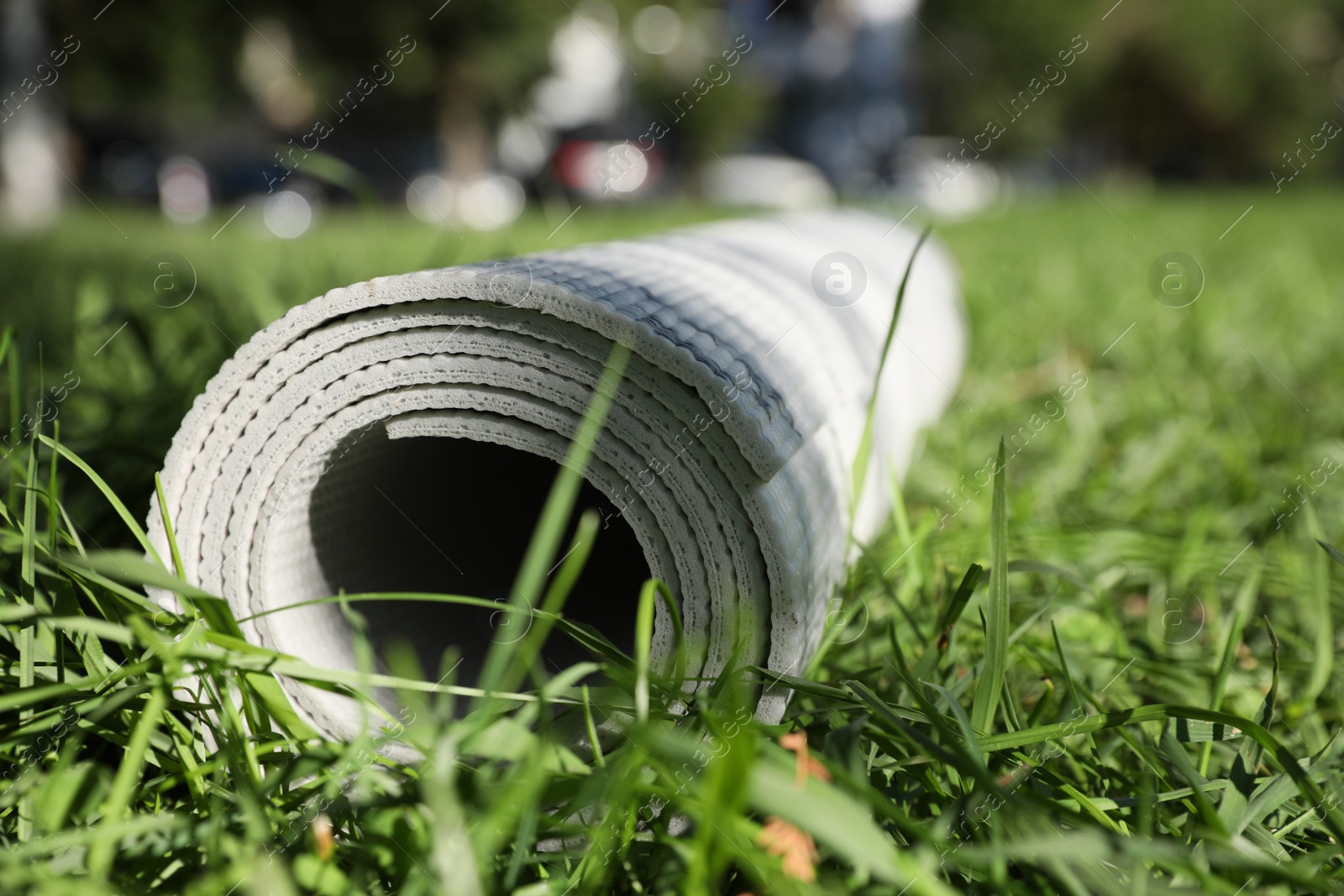 Photo of Rolled karemat or fitness mat on green grass outdoors, closeup. Space for text