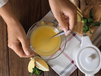 Photo of Woman making aromatic ginger tea at wooden table, top view
