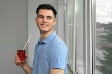 Handsome young man with glass of juice near window at home