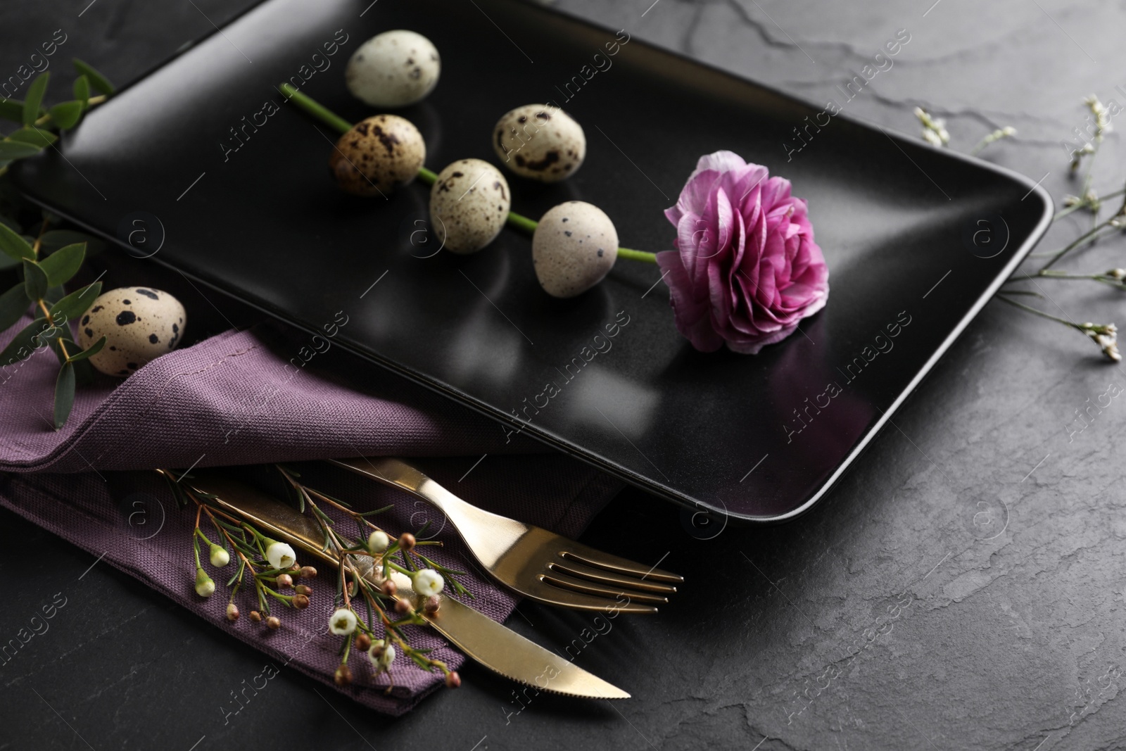 Photo of Festive Easter table setting with quail eggs and floral decoration on dark background, closeup