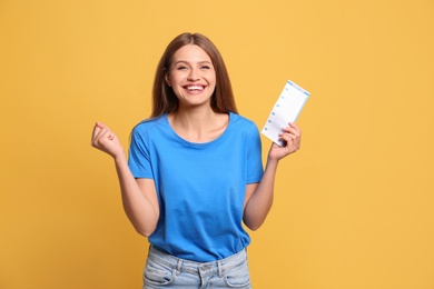 Portrait of happy young woman with lottery ticket on yellow background