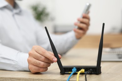 Photo of Man with smartphone and laptop connecting to internet via Wi-Fi router at wooden table, closeup