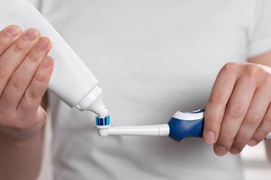 Photo of Woman squeezing toothpaste from tube onto electric toothbrush, closeup