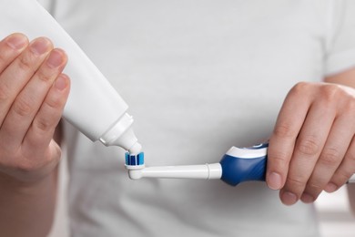 Woman squeezing toothpaste from tube onto electric toothbrush, closeup