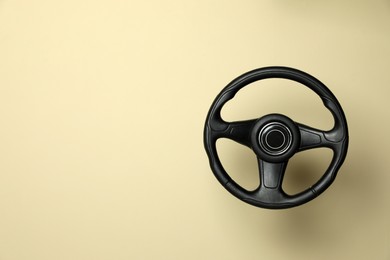 Photo of New black steering wheel on beige background, space for text