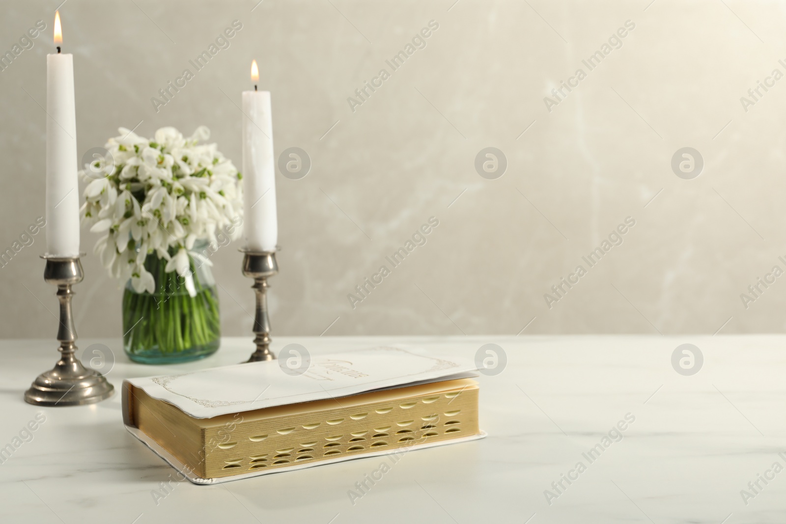 Photo of Burning church candles, Bible and flowers on white marble table. Space for text