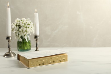 Burning church candles, Bible and flowers on white marble table. Space for text