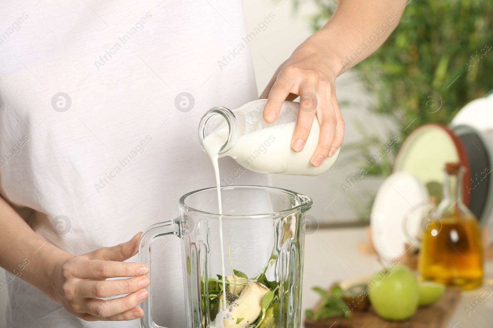 Photo of Woman adding milk into blender with ingredients for green smoothie, closeup