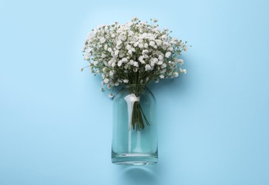 Photo of Bouquet of white gypsophila in glass vase on light blue background, top view