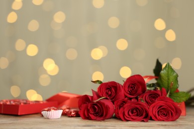 Beautiful red roses and candies on table against blurred lights, space for text. St. Valentine's day celebration
