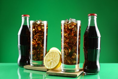 Photo of Bottles and glasses of refreshing soda water on green background