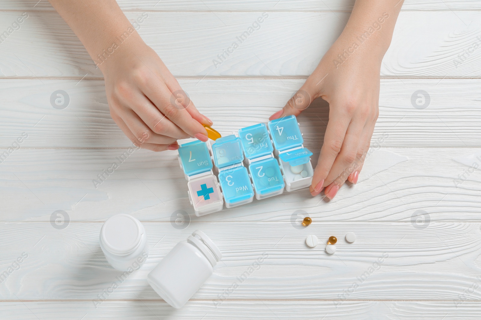 Photo of Woman putting pill into weekly organizer at wooden white table, top view