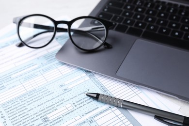 Tax forms, pen, glasses and laptop on table, closeup