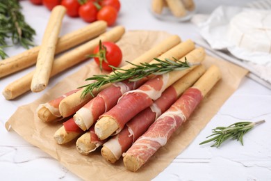 Delicious grissini sticks with prosciutto on white table