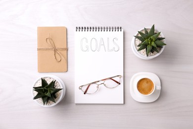Notebook with word Goals, houseplants, glasses and cup of coffee on white wooden table, flat lay. Planning concept