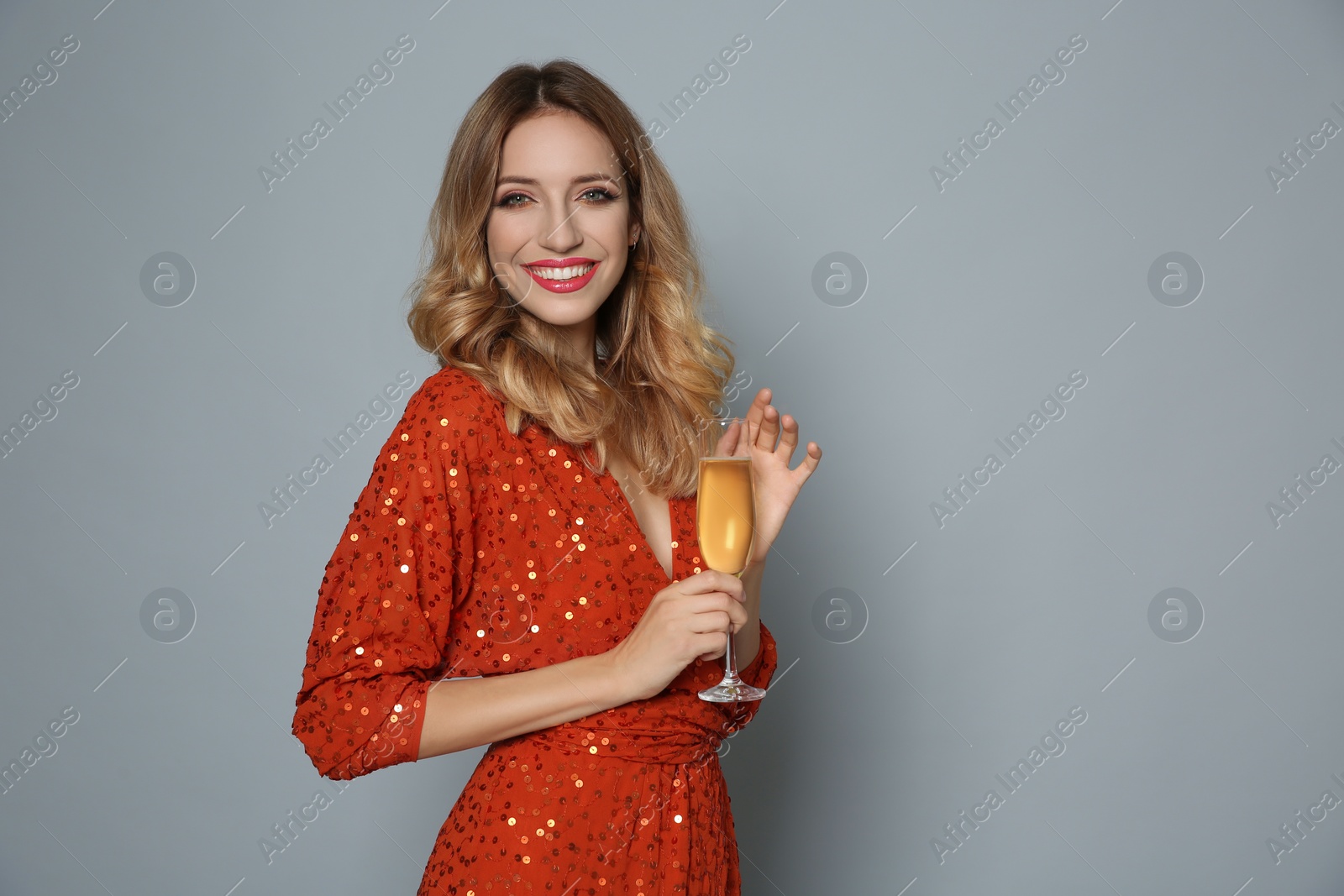 Photo of Happy woman in shiny dress with glass of champagne on grey background, space for text. Christmas party