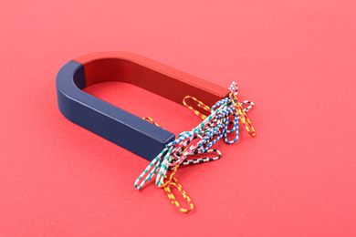 Photo of Magnet attracting paper clips on red background