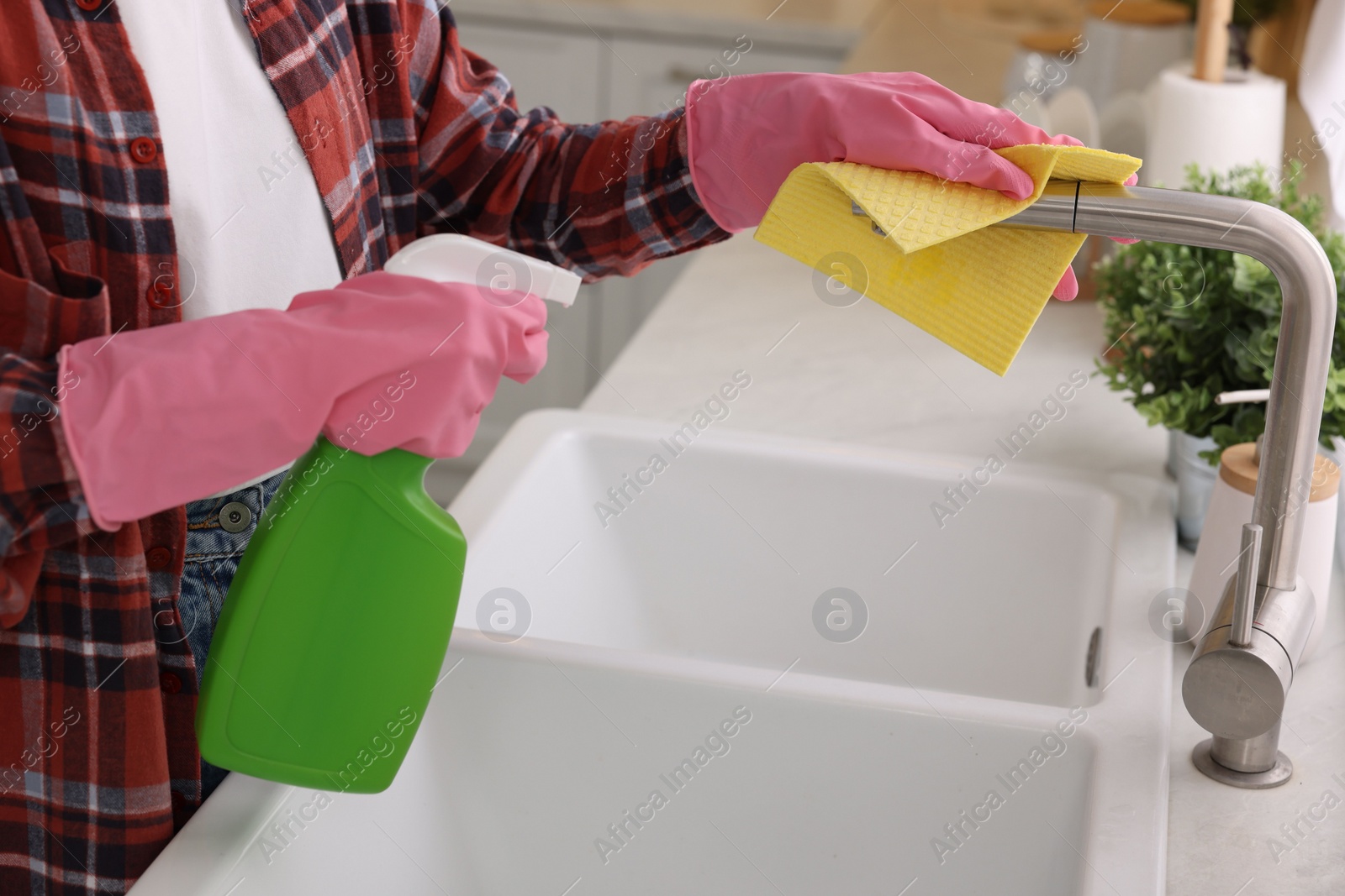 Photo of Woman with spray bottle and microfiber cloth cleaning water tap in kitchen, closeup