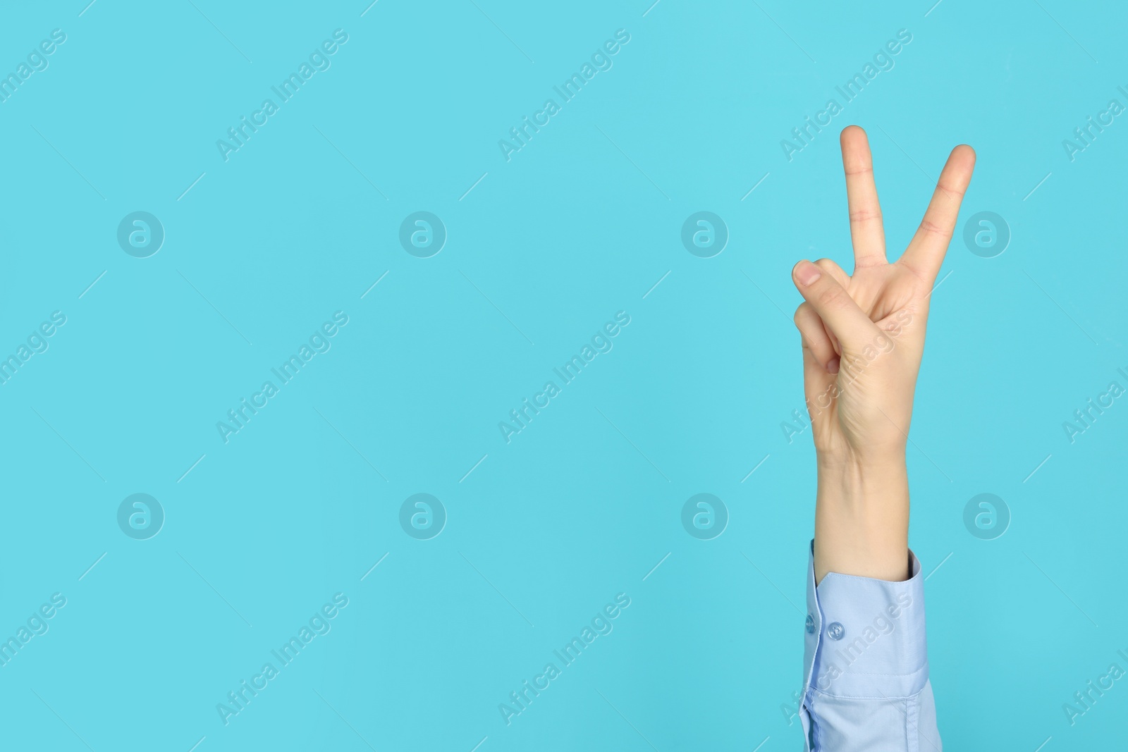 Photo of Young woman showing victory gesture on color background. Space for text