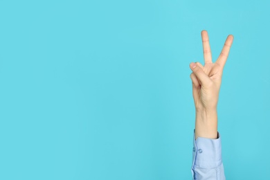 Photo of Young woman showing victory gesture on color background. Space for text