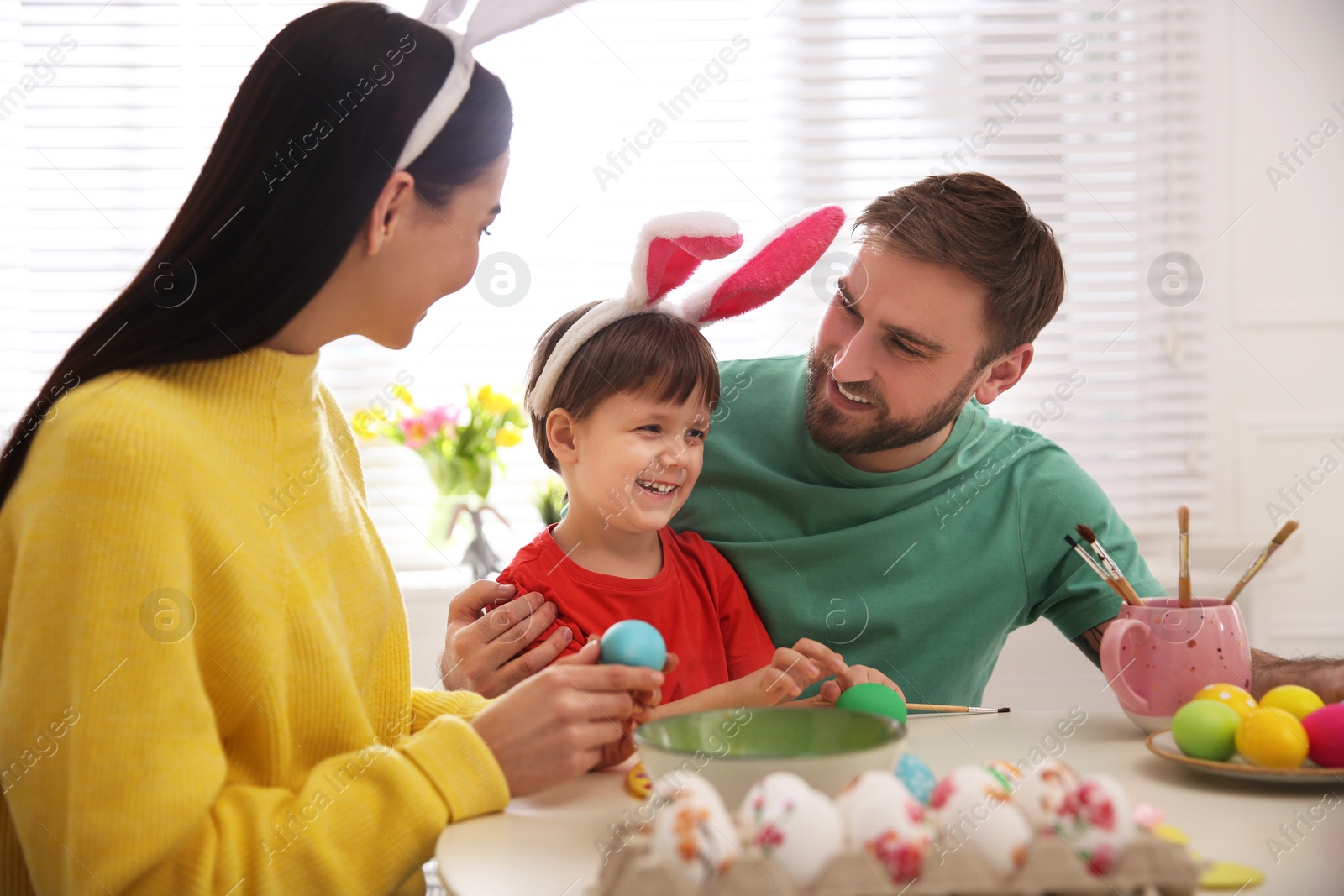 Photo of Happy family painting Easter eggs at table indoors