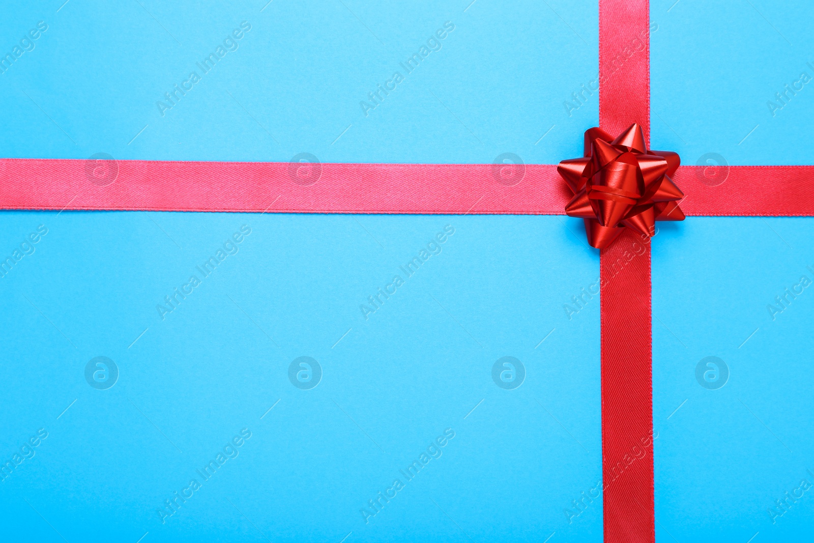 Photo of Red ribbons with bow on light blue background, top view. Space for text