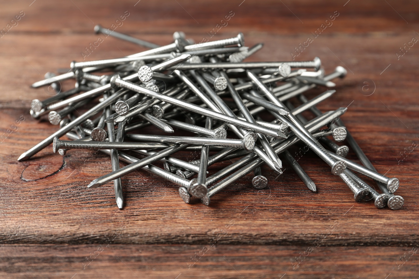 Photo of Pile of metal nails on wooden background, closeup