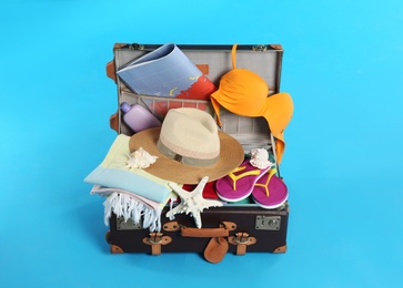 Photo of Open vintage suitcase with different beach objects packed for summer vacation on light blue background