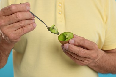 Photo of Man eating kiwi with spoon on light blue background, closeup