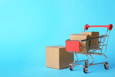 Photo of Shopping cart and boxes on light blue background, space for text. Logistics and wholesale concept