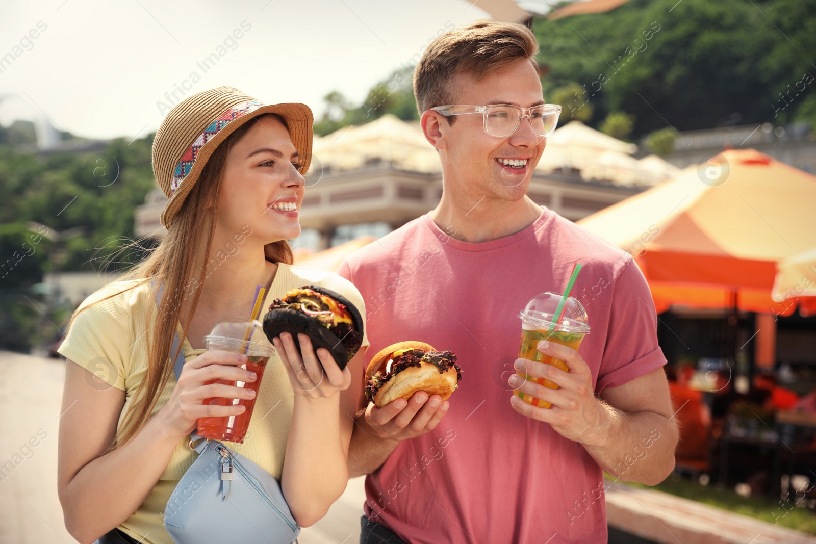 Photo of Young happy couple with burgers walking on city street