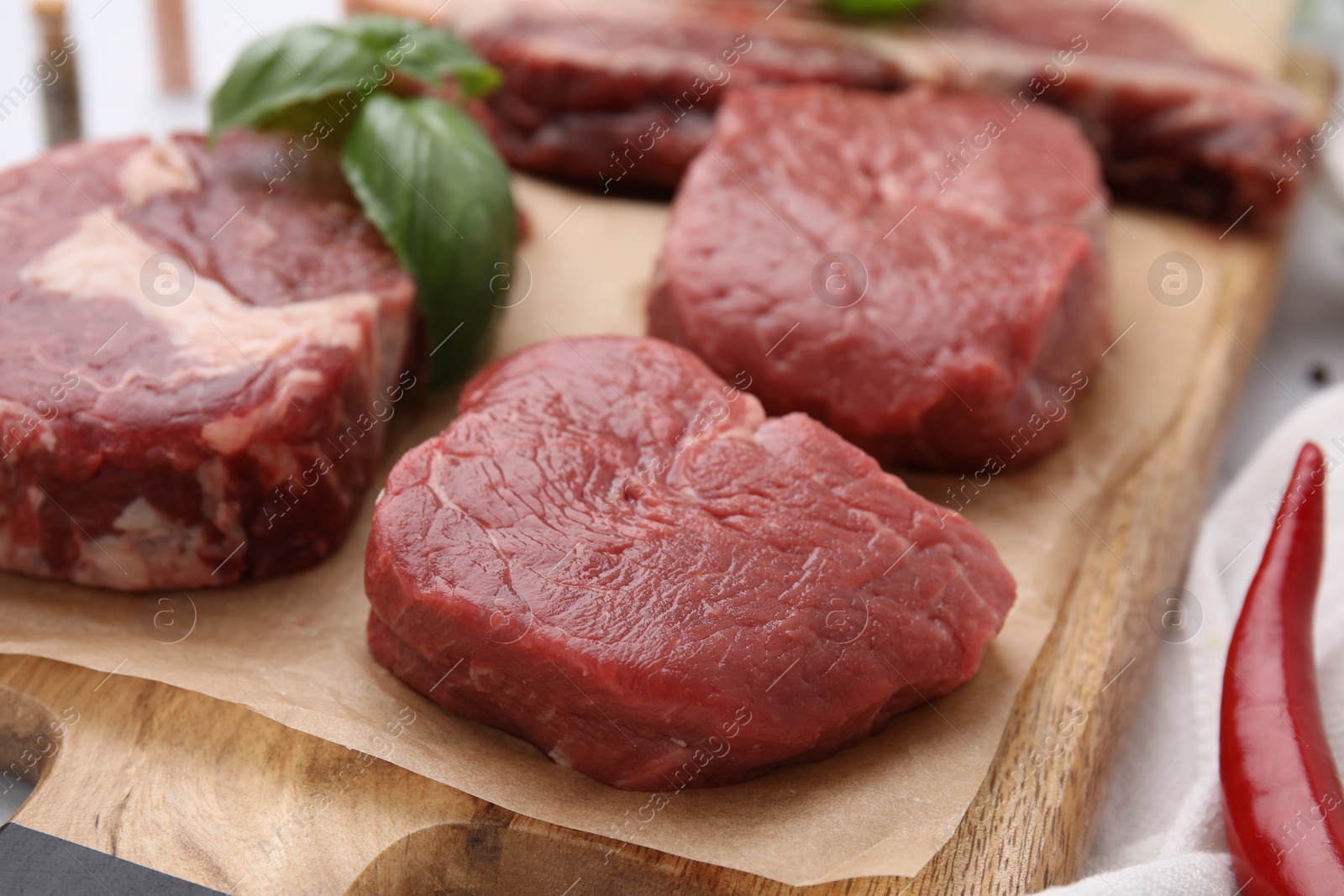 Photo of Cut fresh beef meat with basil leaves on wooden board, closeup