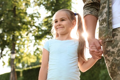 Father in military uniform walking with his daughter at sunny park