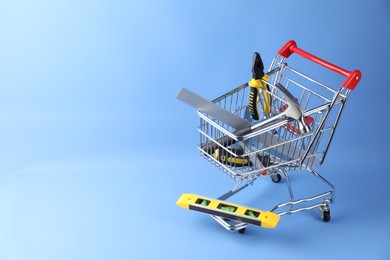 Photo of Small shopping cart with set of construction tools on light blue background. Space for text