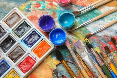 Photo of Different brushes and paints on color palette, top view