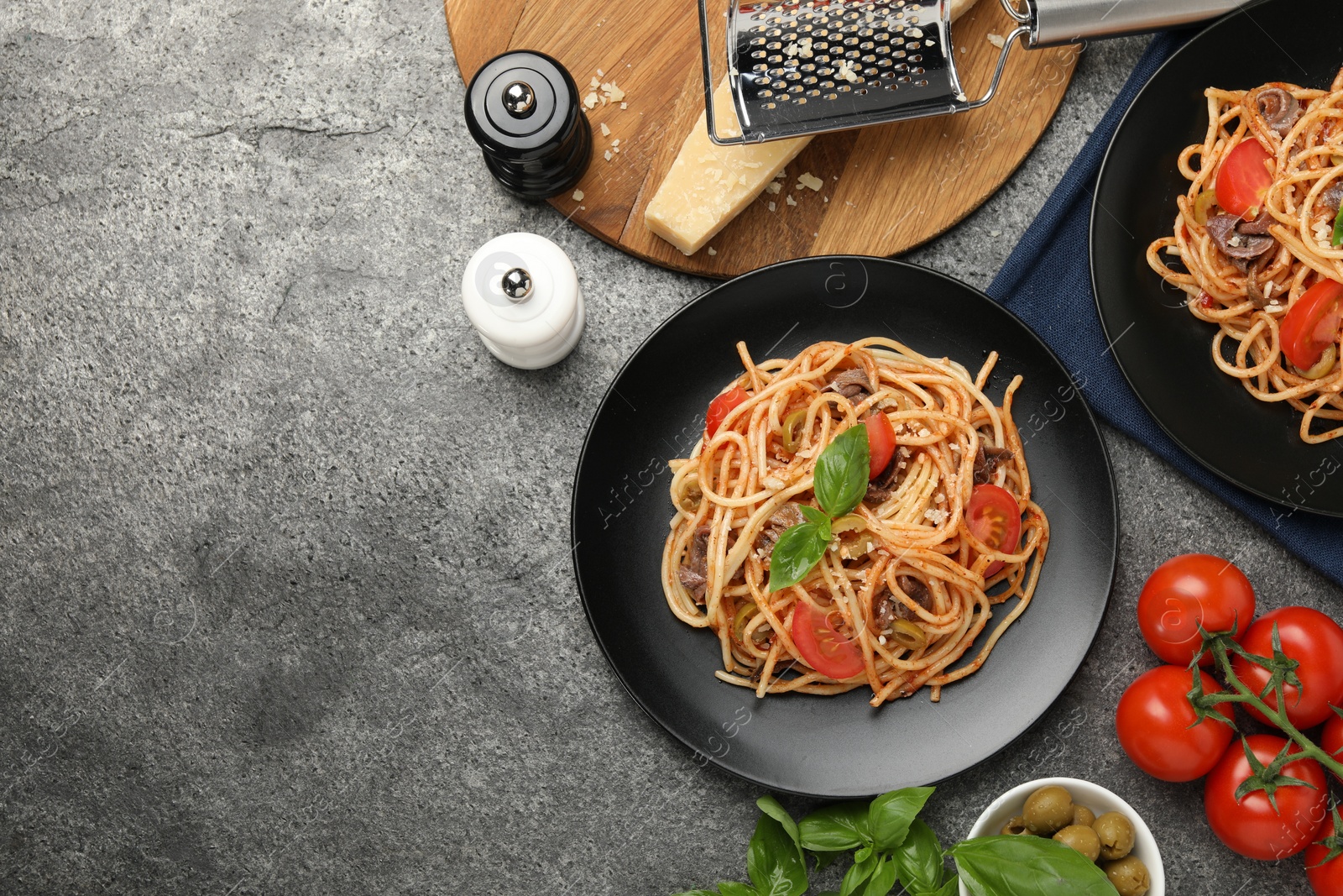 Photo of Delicious pasta with anchovies, tomatoes and olives on grey table, flat lay. Space for text