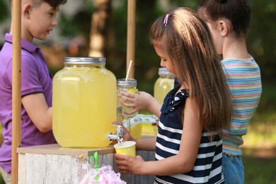 Photo of Cute little girl pouring natural lemonade into cup in park. Summer refreshing drink