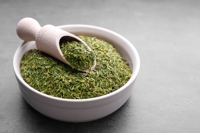 Photo of Bowl and scoop with dried thyme on grey table, closeup