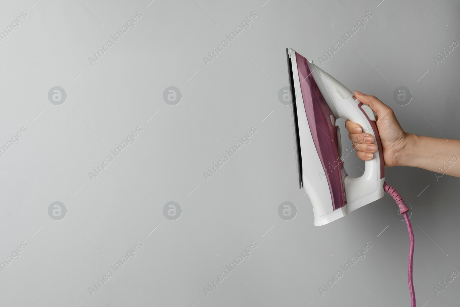 Photo of Woman holding modern iron on light grey background, closeup. Space for text