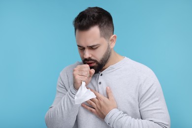 Photo of Sick man with tissue coughing on light blue background
