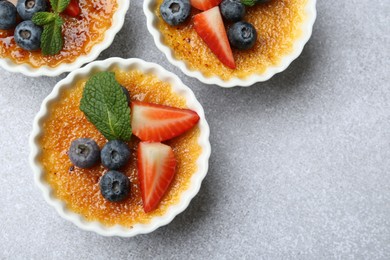 Photo of Delicious creme brulee with berries and mint in bowl on grey textured table, top view
