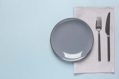 Photo of Clean plate and shiny silver cutlery on light grey background, flat lay. Space for text