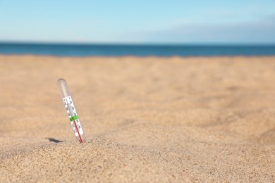 Photo of Weather thermometer in sand near sea, space for text