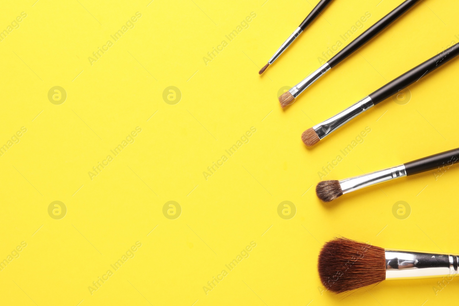 Photo of Set of makeup brushes on yellow background, flat lay. Space for text