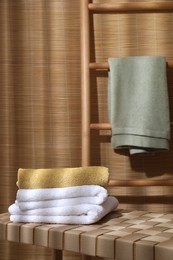 Photo of Stacked soft towels on wicker bench indoors